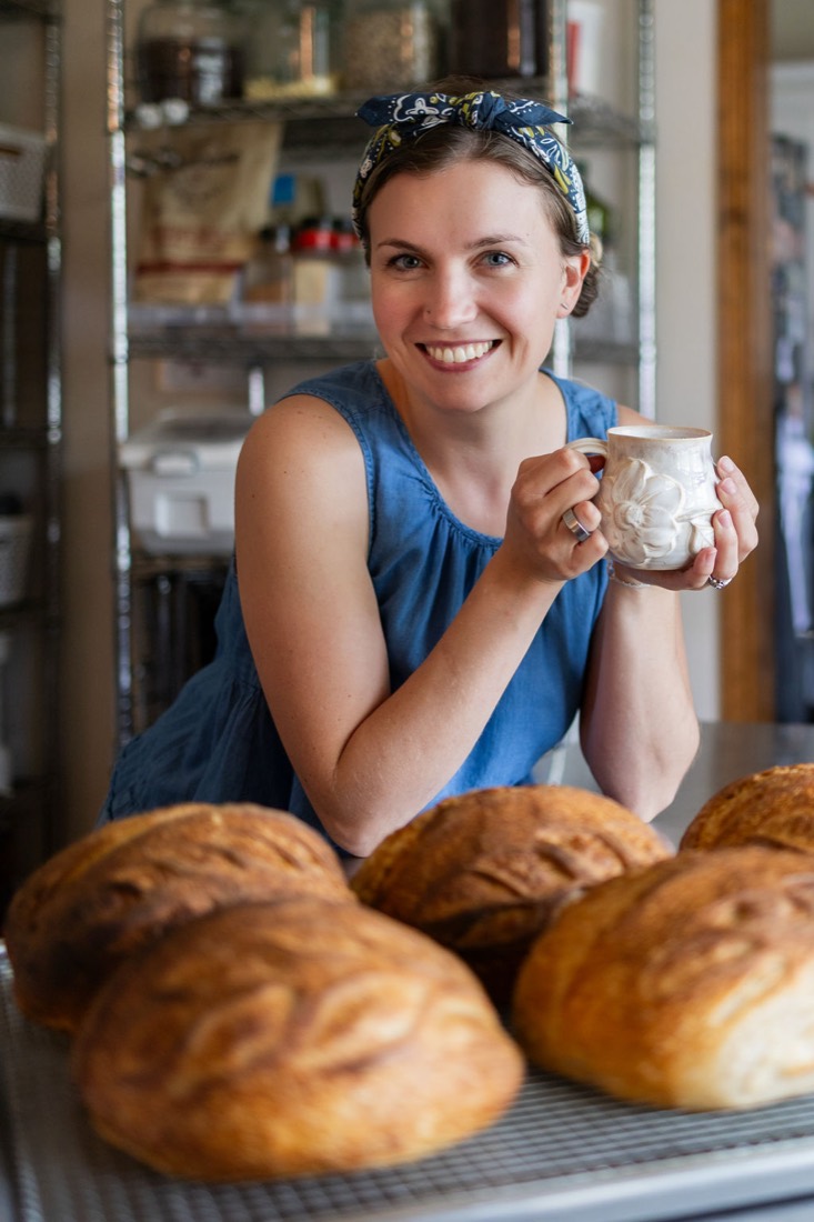 Caroline with her coffee behind a bench of fresh loaves